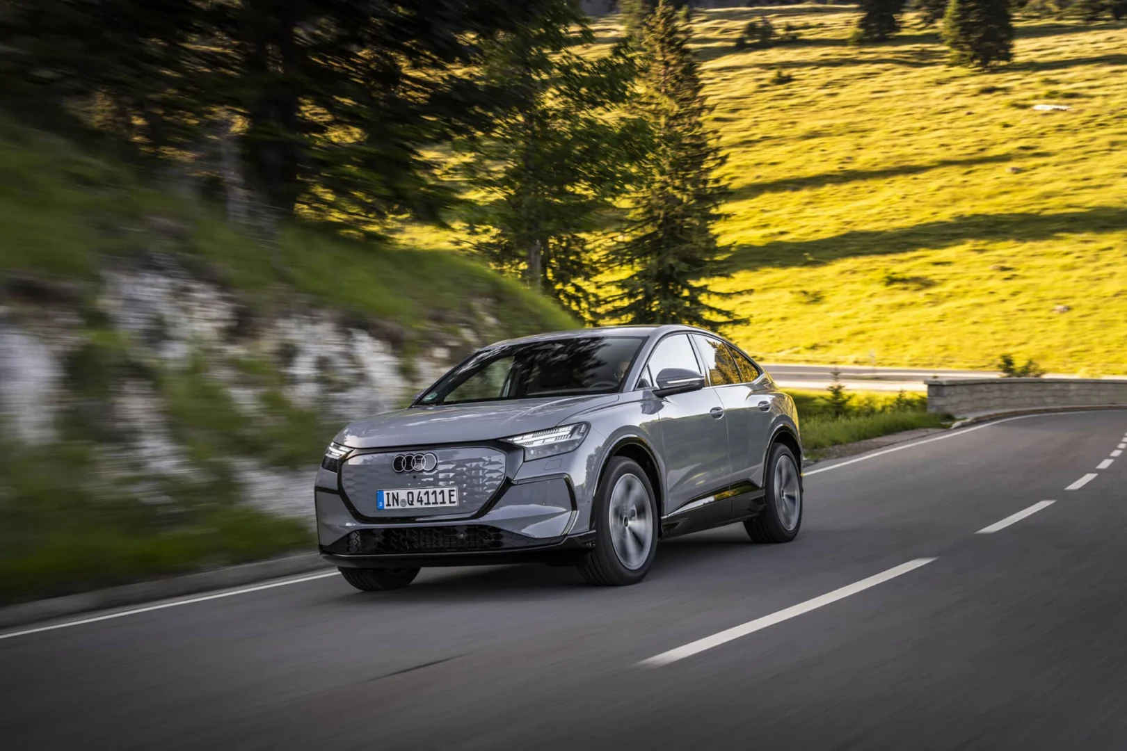 The right car for any situation: the Audi Q4 e-tron takes to the streets - Audi Q4 Sportback e-tron in Pebble grey, outdoor driving shot, exterior, three-quarter front view on a winding country road in a mountainous landscape.