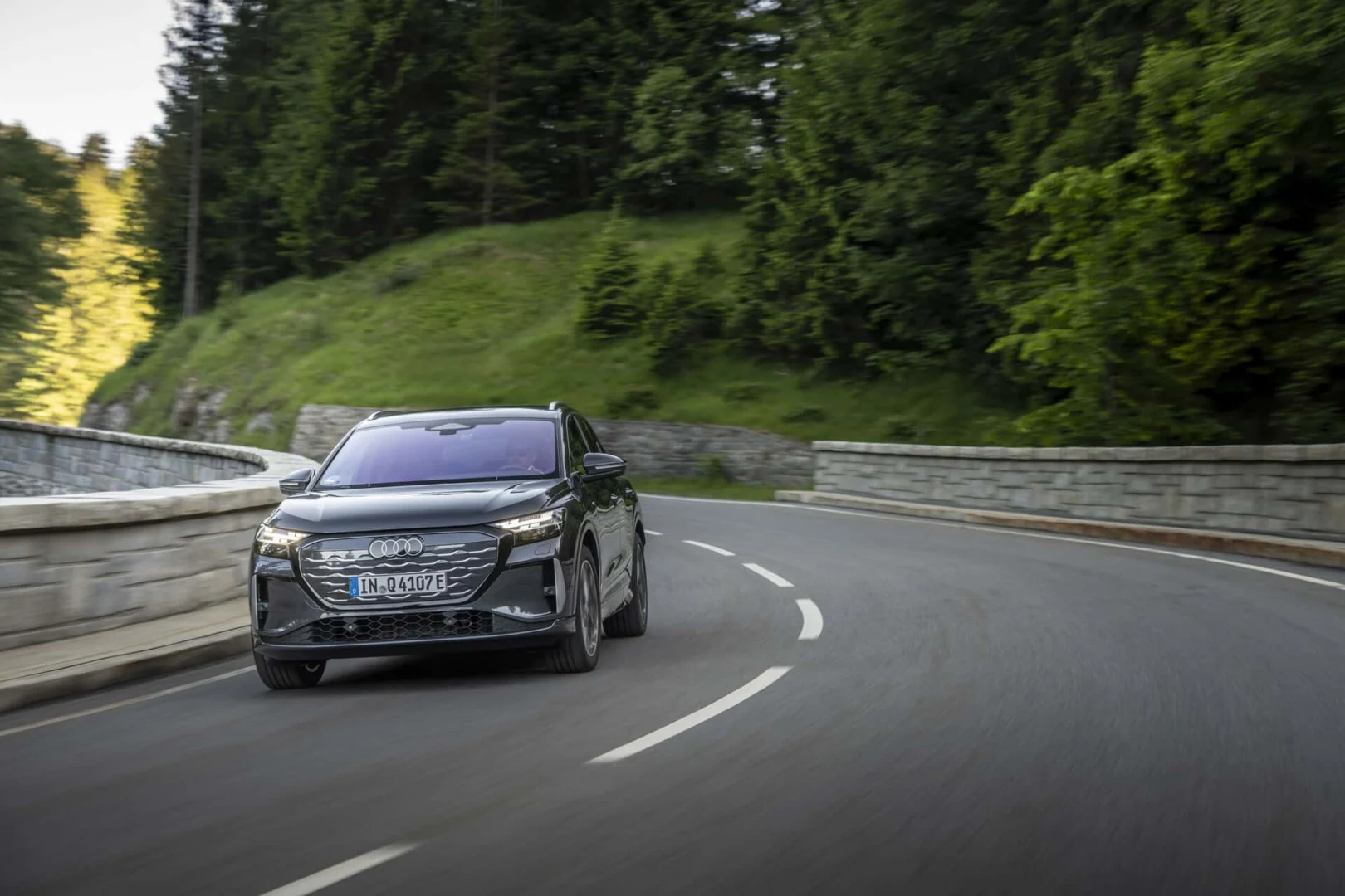 The right car for any situation: the Audi Q4 e-tron takes to the streets - Audi Q4 SUV e-tron in Tamboragrey, outdoor driving shot, exterior, front view on a winding road in a forested landscape.