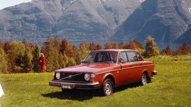 1975 červené 244 GL zaparkované v tráve s horami v pozadí.